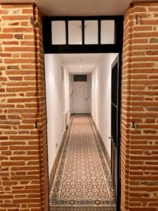 Rénovation d’un mur en brique ouvrant sur un couloir peint, avec pose de carrelage respectant le charme ancien de la maison